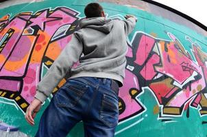 A young guy in a gray hoodie paints graffiti in pink and green c photo