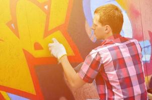 A young red-haired graffiti artist paints a new graffiti on the wall. Photo of the process of drawing a graffiti on a wall close-up. The concept of street art and illegal vandalism