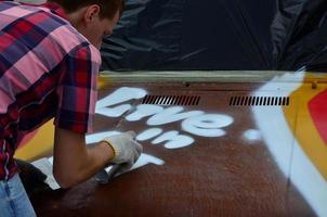 un joven grafitero pelirrojo pinta un nuevo grafiti colorido en el camión. foto del proceso de dibujo de un grafiti en el primer plano de un coche. el concepto de arte callejero y vandalismo ilegal