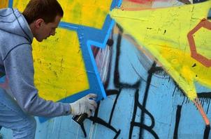 A young red-haired graffiti artist paints a new graffiti on the wall. Photo of the process of drawing a graffiti on a wall close-up. The concept of street art and illegal vandalism