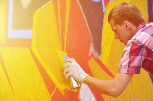 A young red-haired graffiti artist paints a new graffiti on the wall. Photo of the process of drawing a graffiti on a wall close-up. The concept of street art and illegal vandalism