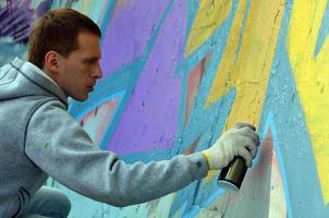 A young red-haired graffiti artist paints a new graffiti on the wall. Photo of the process of drawing a graffiti on a wall close-up. The concept of street art and illegal vandalism