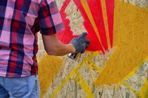 A hand with a spray can that draws a new graffiti on the wall. Photo of the process of drawing a graffiti on a wooden wall close-up. The concept of street art and illegal vandalism