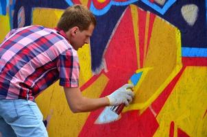 A young red-haired graffiti artist paints a new graffiti on the wall. Photo of the process of drawing a graffiti on a wall close-up. The concept of street art and illegal vandalism