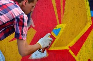 A young red-haired graffiti artist paints a new graffiti on the wall. Photo of the process of drawing a graffiti on a wall close-up. The concept of street art and illegal vandalism