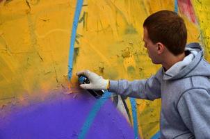 A young red-haired graffiti artist paints a new graffiti on the wall. Photo of the process of drawing a graffiti on a wall close-up. The concept of street art and illegal vandalism