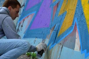 A young red-haired graffiti artist paints a new graffiti on the wall. Photo of the process of drawing a graffiti on a wall close-up. The concept of street art and illegal vandalism