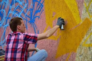 A young red-haired graffiti artist paints a new graffiti on the wall. Photo of the process of drawing a graffiti on a wall close-up. The concept of street art and illegal vandalism