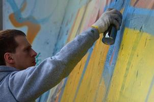 A young red-haired graffiti artist paints a new graffiti on the wall. Photo of the process of drawing a graffiti on a wall close-up. The concept of street art and illegal vandalism