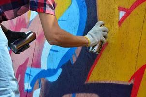 A hand with a spray can that draws a new graffiti on the wall. Photo of the process of drawing a graffiti on a wooden wall close-up. The concept of street art and illegal vandalism