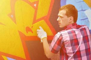 A young red-haired graffiti artist paints a new graffiti on the wall. Photo of the process of drawing a graffiti on a wall close-up. The concept of street art and illegal vandalism