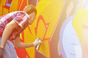 A young red-haired graffiti artist paints a new graffiti on the wall. Photo of the process of drawing a graffiti on a wall close-up. The concept of street art and illegal vandalism