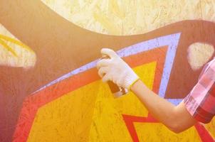 A hand with a spray can that draws a new graffiti on the wall. Photo of the process of drawing a graffiti on a wooden wall close-up. The concept of street art and illegal vandalism