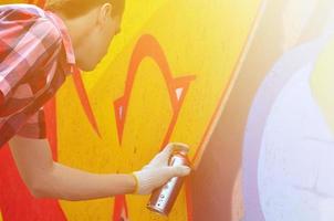 A young red-haired graffiti artist paints a new graffiti on the wall. Photo of the process of drawing a graffiti on a wall close-up. The concept of street art and illegal vandalism