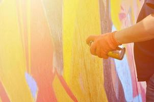 A hand with a spray can that draws a new graffiti on the wall. Photo of the process of drawing a graffiti on a wooden wall close-up. The concept of street art and illegal vandalism