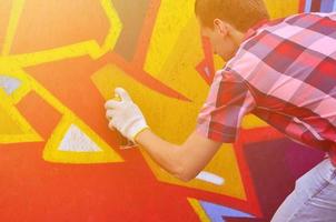 A young red-haired graffiti artist paints a new graffiti on the wall. Photo of the process of drawing a graffiti on a wall close-up. The concept of street art and illegal vandalism
