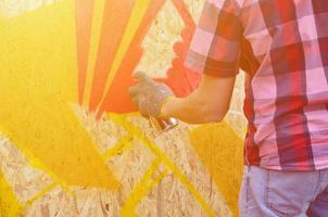 una mano con un bote de spray que dibuja un nuevo grafiti en la pared. foto del proceso de dibujar un graffiti en un primer plano de la pared de madera. el concepto de arte callejero y vandalismo ilegal