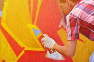 A young red-haired graffiti artist paints a new graffiti on the wall. Photo of the process of drawing a graffiti on a wall close-up. The concept of street art and illegal vandalism