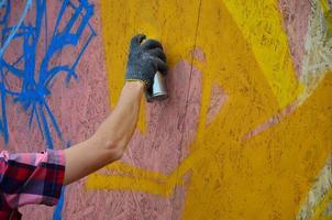 A hand with a spray can that draws a new graffiti on the wall. Photo of the process of drawing a graffiti on a wooden wall close-up. The concept of street art and illegal vandalism