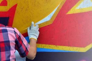 A hand with a spray can that draws a new graffiti on the wall. Photo of the process of drawing a graffiti on a wooden wall close-up. The concept of street art and illegal vandalism