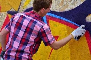 A young red-haired graffiti artist paints a new graffiti on the wall. Photo of the process of drawing a graffiti on a wall close-up. The concept of street art and illegal vandalism
