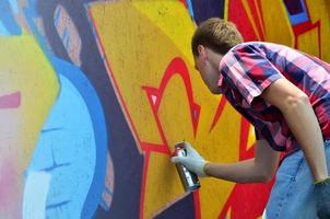 A young red-haired graffiti artist paints a new graffiti on the wall. Photo of the process of drawing a graffiti on a wall close-up. The concept of street art and illegal vandalism