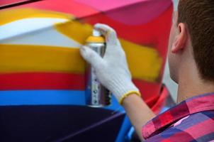 un joven grafitero pelirrojo pinta un nuevo grafiti colorido en el camión. foto del proceso de dibujo de un grafiti en el primer plano de un coche. el concepto de arte callejero y vandalismo ilegal