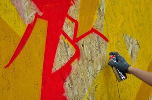 A hand with a spray can that draws a new graffiti on the wall. Photo of the process of drawing a graffiti on a wooden wall close-up. The concept of street art and illegal vandalism