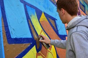 un joven grafitero pelirrojo pinta un nuevo grafiti en la pared. foto del proceso de dibujar un graffiti en un primer plano de la pared. el concepto de arte callejero y vandalismo ilegal