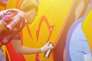 A young red-haired graffiti artist paints a new graffiti on the wall. Photo of the process of drawing a graffiti on a wall close-up. The concept of street art and illegal vandalism