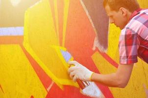 un joven grafitero pelirrojo pinta un nuevo grafiti en la pared. foto del proceso de dibujar un graffiti en un primer plano de la pared. el concepto de arte callejero y vandalismo ilegal