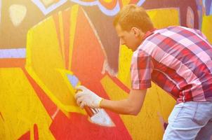 A young red-haired graffiti artist paints a new graffiti on the wall. Photo of the process of drawing a graffiti on a wall close-up. The concept of street art and illegal vandalism