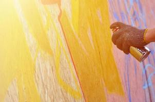 A hand with a spray can that draws a new graffiti on the wall. Photo of the process of drawing a graffiti on a wooden wall close-up. The concept of street art and illegal vandalism