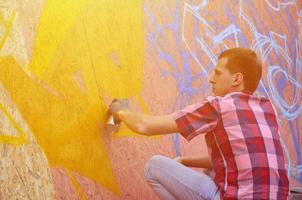 A young red-haired graffiti artist paints a new graffiti on the wall. Photo of the process of drawing a graffiti on a wall close-up. The concept of street art and illegal vandalism