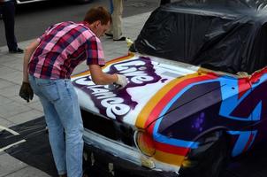 A young red-haired graffiti artist paints a new colorful graffiti on the car. Photo of the process of drawing a graffiti on a car close-up. The concept of street art and illegal vandalism