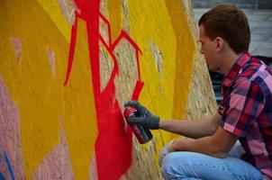 A young red-haired graffiti artist paints a new graffiti on the wall. Photo of the process of drawing a graffiti on a wall close-up. The concept of street art and illegal vandalism