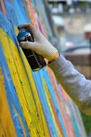 A hand with a spray can that draws a new graffiti on the wall. Photo of the process of drawing a graffiti on a concrete wall close-up. The concept of street art and illegal vandalism