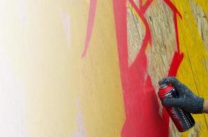 A hand with a spray can that draws a new graffiti on the wall. Photo of the process of drawing a graffiti on a wooden wall close-up. The concept of street art and illegal vandalism