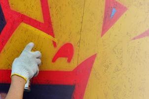 A hand with a spray can that draws a new graffiti on the wall. Photo of the process of drawing a graffiti on a wooden wall close-up. The concept of street art and illegal vandalism