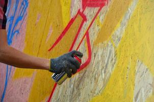 A hand with a spray can that draws a new graffiti on the wall. Photo of the process of drawing a graffiti on a wooden wall close-up. The concept of street art and illegal vandalism