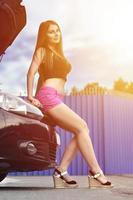 Girl in pink shorts with wrenches near a black car with an open photo