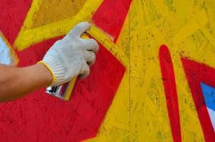 A hand with a spray can that draws a new graffiti on the wall. Photo of the process of drawing a graffiti on a wooden wall close-up. The concept of street art and illegal vandalism