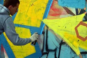 A young red-haired graffiti artist paints a new graffiti on the wall. Photo of the process of drawing a graffiti on a wall close-up. The concept of street art and illegal vandalism