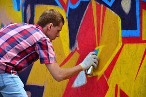 A young red-haired graffiti artist paints a new graffiti on the wall. Photo of the process of drawing a graffiti on a wall close-up. The concept of street art and illegal vandalism