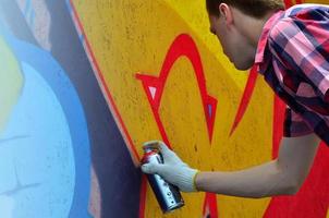 A young red-haired graffiti artist paints a new graffiti on the wall. Photo of the process of drawing a graffiti on a wall close-up. The concept of street art and illegal vandalism