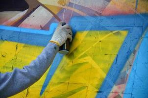 A hand with a spray can that draws a new graffiti on the wall. Photo of the process of drawing a graffiti on a concrete wall close-up. The concept of street art and illegal vandalism