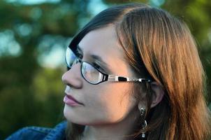 Girl in glasses and jeans jacket is resting on the roof of a hou photo