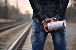 Girl in handcuffs with spraycan on the background of a railway track. The concept of vandalism prevention with the participation of the railway and trains. photo