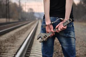 la chica esposada con la llave ajustable en el fondo de la vía férrea. el concepto de prevención del delito con la participación del ferrocarril y los trenes. foto