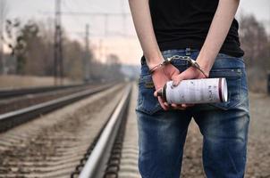 Girl in handcuffs with spraycan on the background of a railway track. The concept of vandalism prevention with the participation of the railway and trains. photo